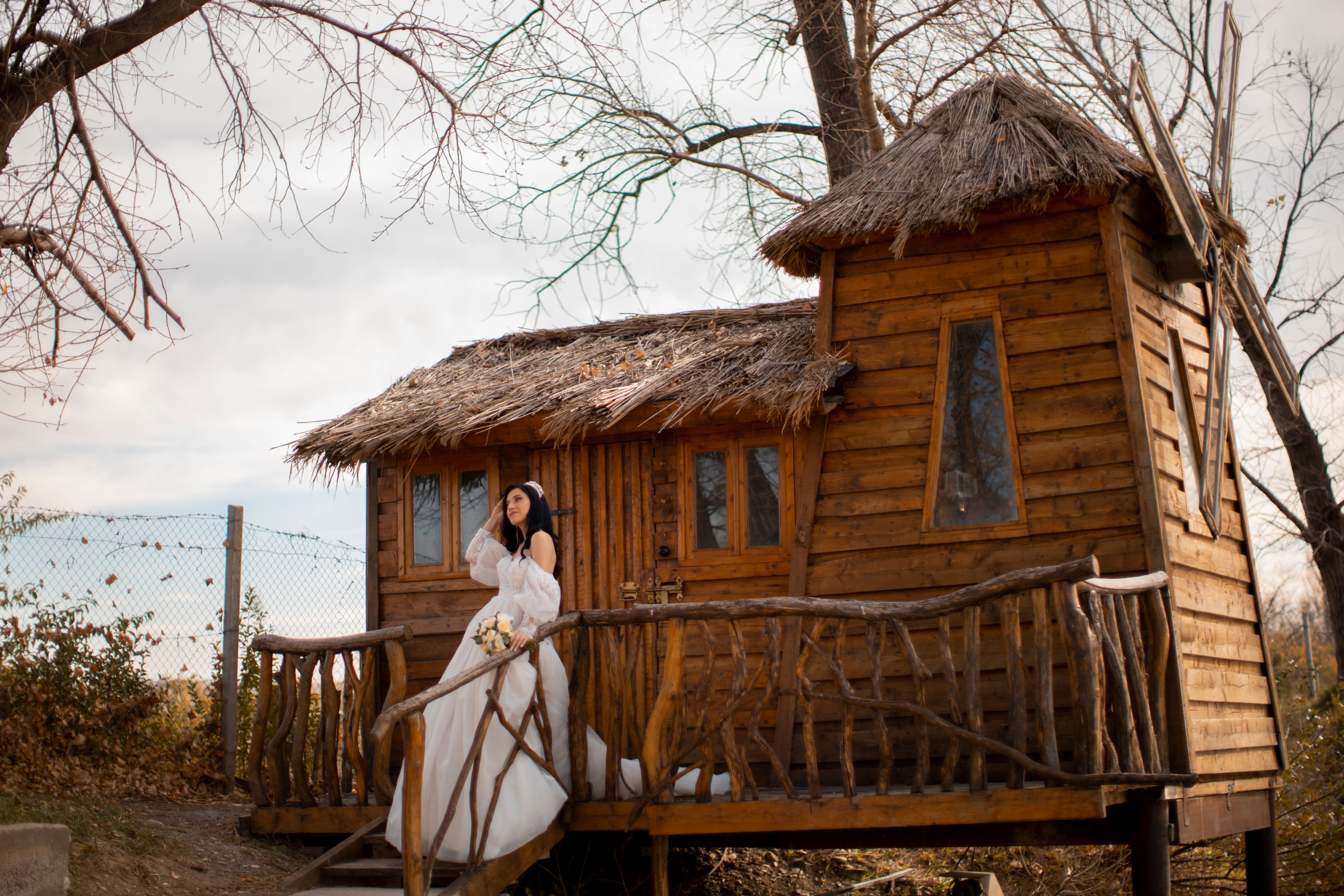 Mariée joyeuse en robe près d’une cabane rustique, ambiance bohème en extérieur