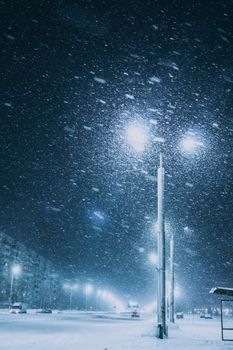 A snowy urban street at night in Vitebsk, Belarus with bright streetlights illuminating falling snow.
