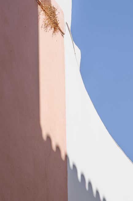 Minimalist architecture with shadows on pastel walls against a blue sky.