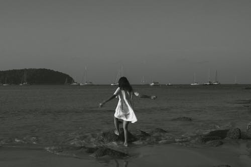 Woman in White Sundress Standing on Rock on Sea Shore in Black and White