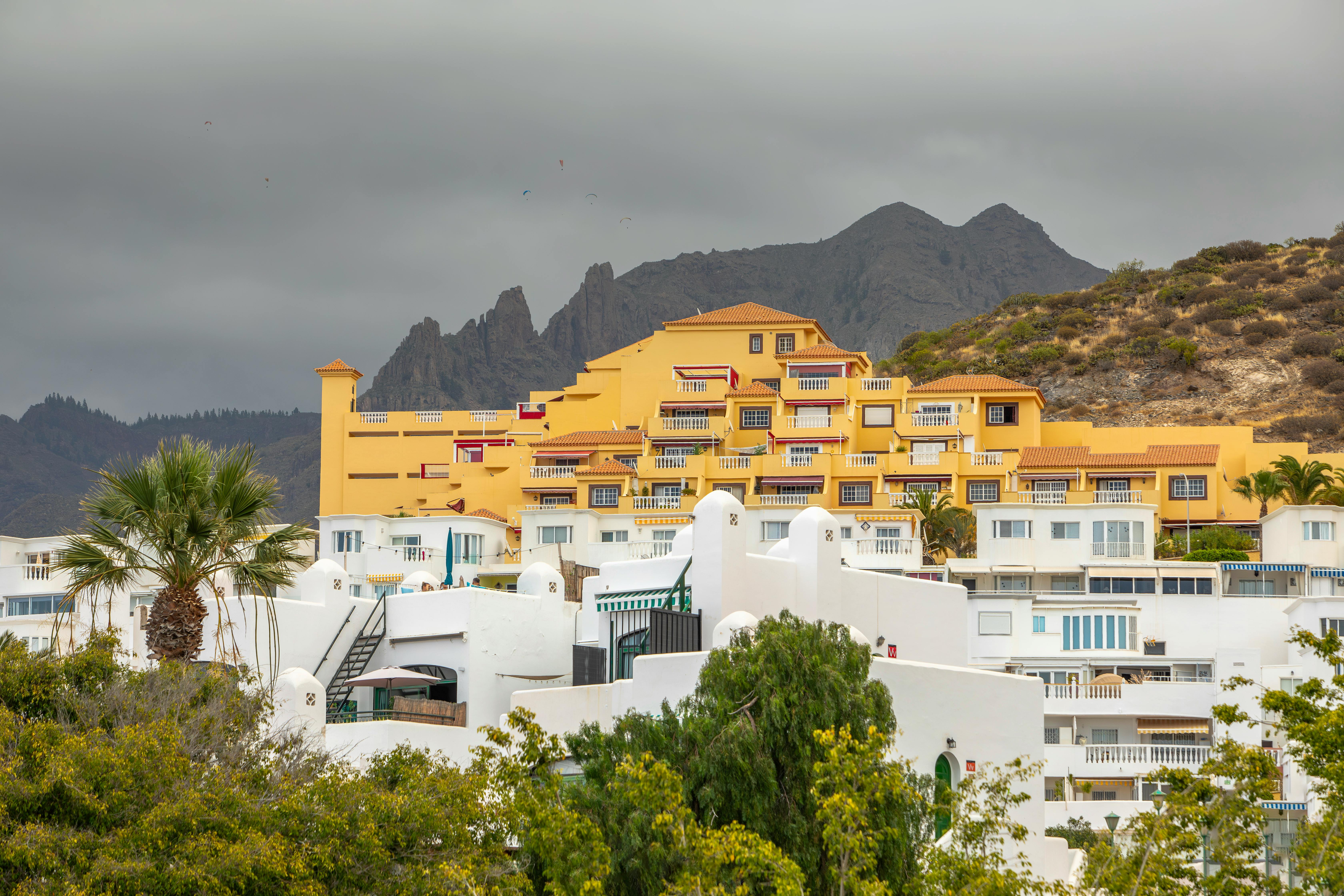 Free Vibrant yellow resort structures amidst a mountainous backdrop under cloudy skies. Stock Photo