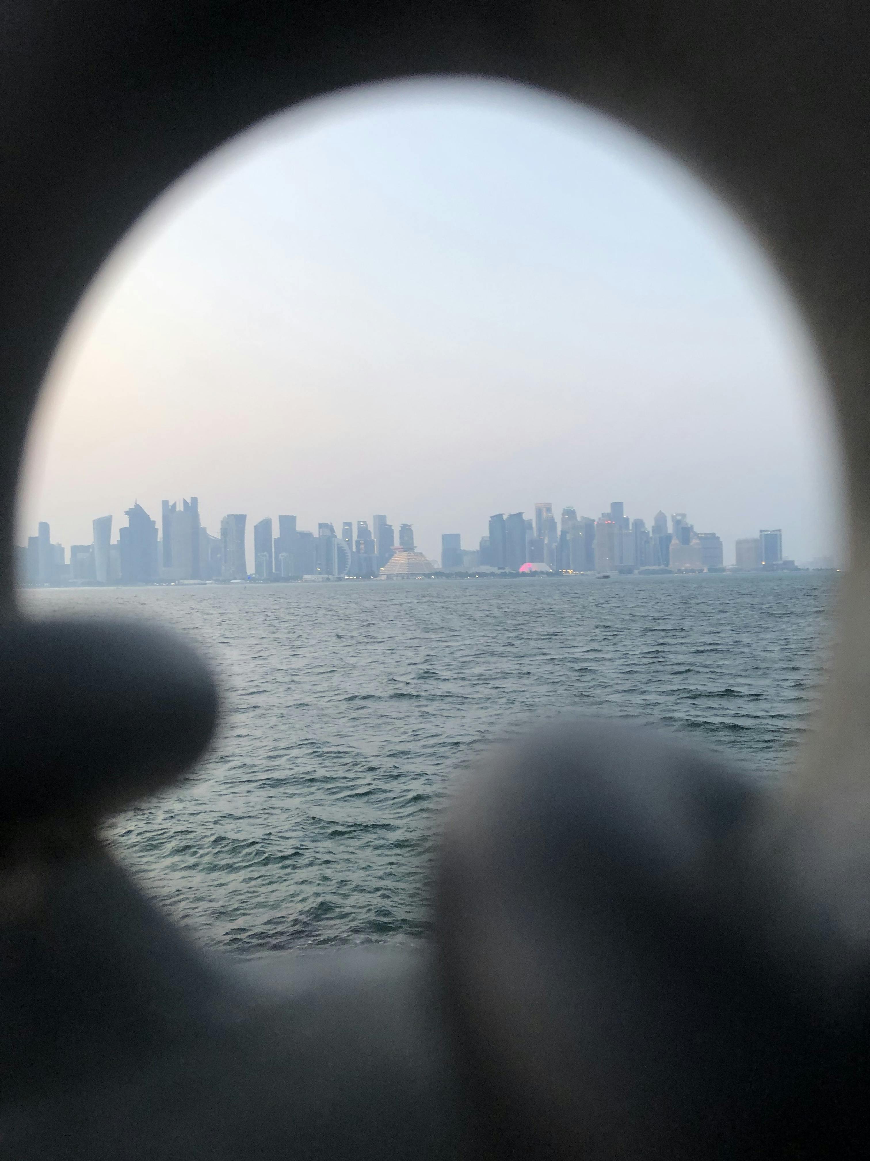 Unique view of Doha's skyline captured through a circular frame over the sea.