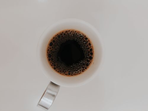 Free Minimalistic top view image of black coffee in a white cup with bubbles on its surface. Stock Photo