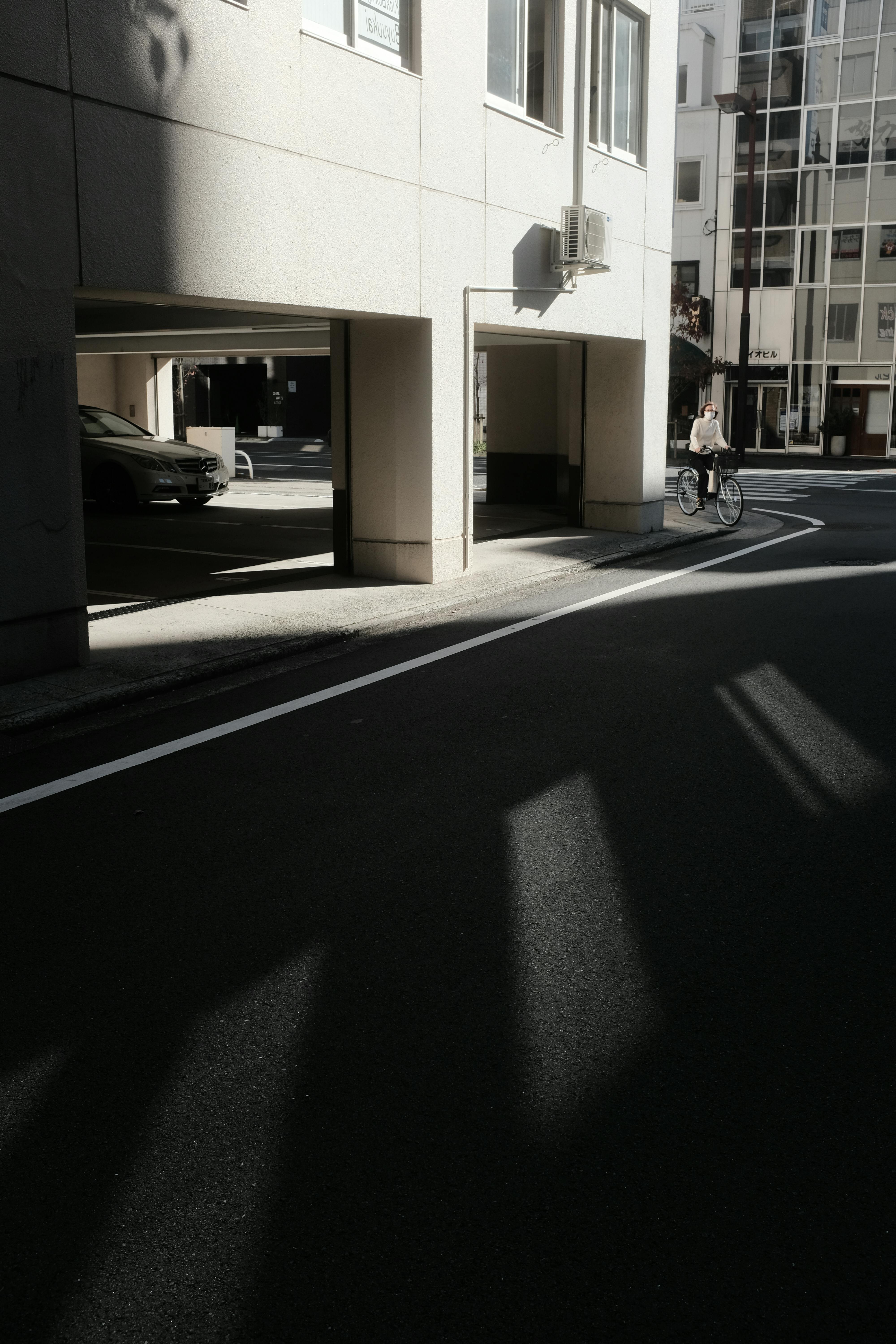 A cyclist rides through a modern urban street, casting long shadows in the sunlight.