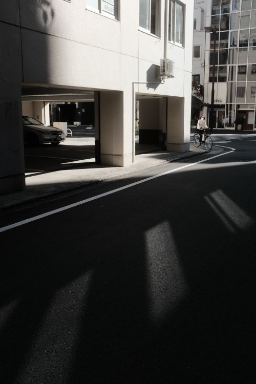 Free A cyclist rides through a modern urban street, casting long shadows in the sunlight. Stock Photo