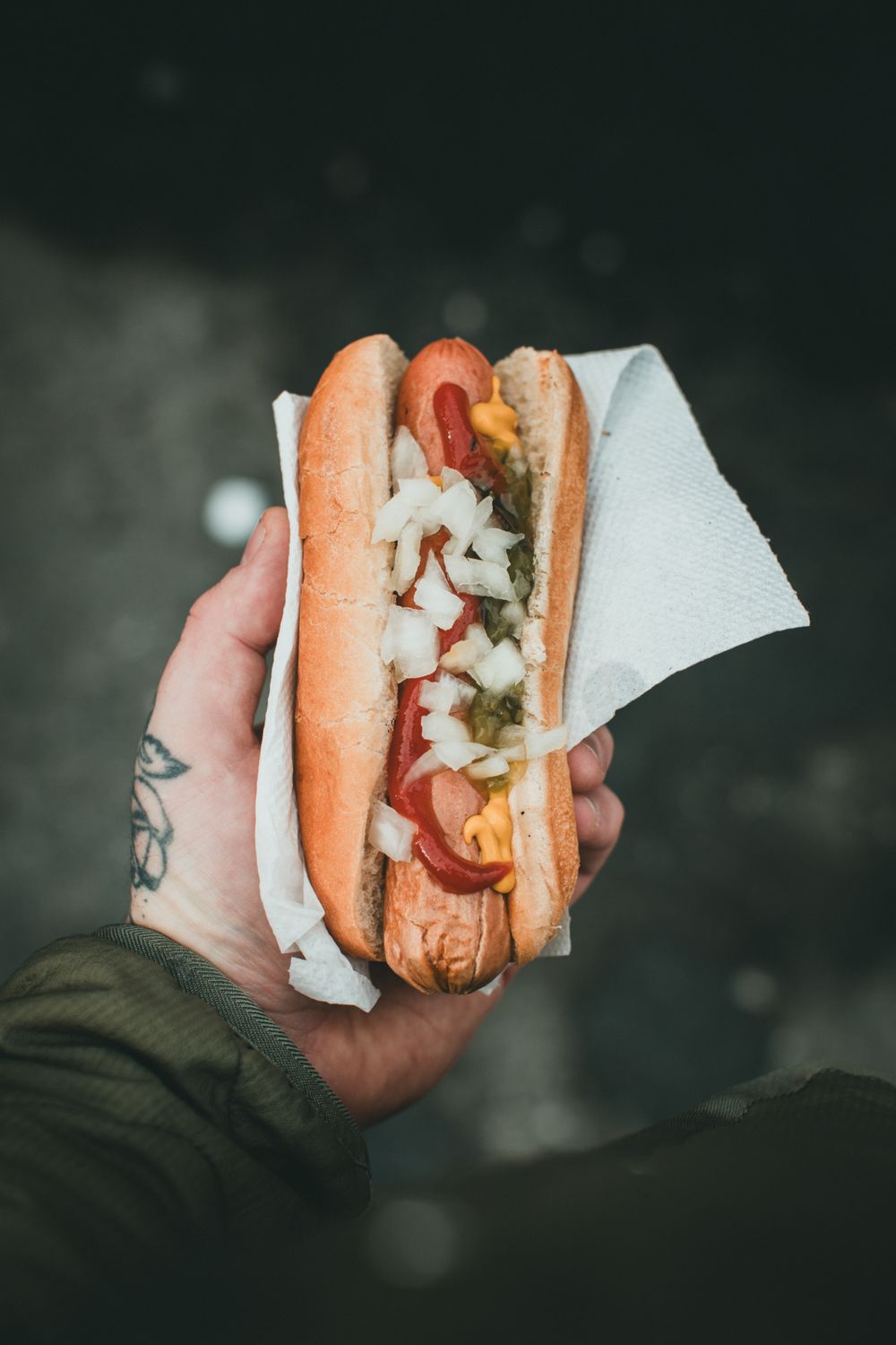 A dressed hot dog with onions and relish, held in a napkin