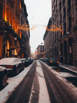 A picturesque snow-covered city street adorned with festive lights during winter.