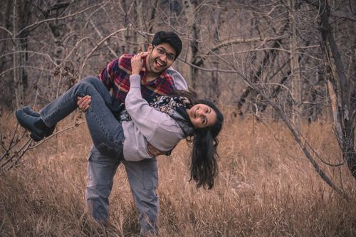 Free A smiling couple enjoys a playful moment in an autumn forest, creating a warm and joyful scene. Stock Photo