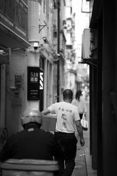 Urban alleyway in black and white featuring pedestrians and building facades, depicting city life.