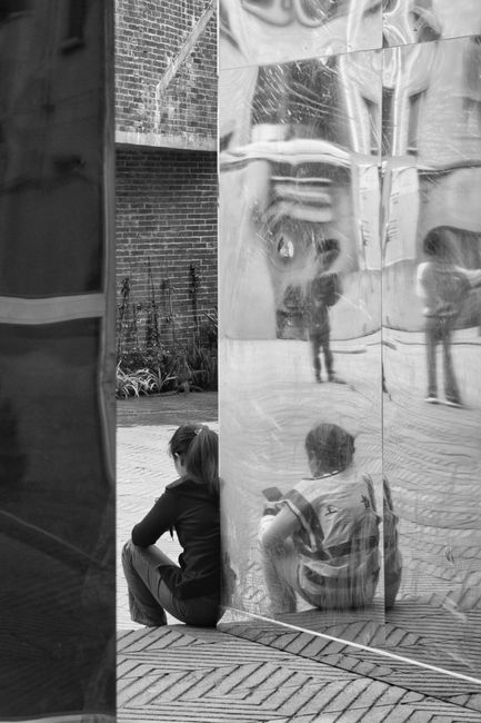 Black and white photo of people beside mirrored urban architecture.