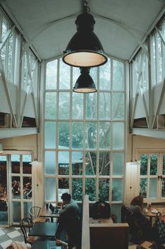 Charming café scene with people seated under a large window and vintage lamp, providing a cozy atmosphere.