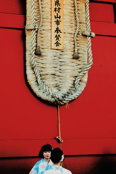 Two women in kimono standing below a large sandal decoration at Taito City temple, Tokyo.
