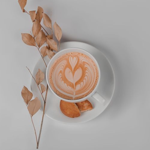 Free Stylish overhead shot of cappuccino with latte art and cookies on white plate, perfect for lifestyle themes. Stock Photo