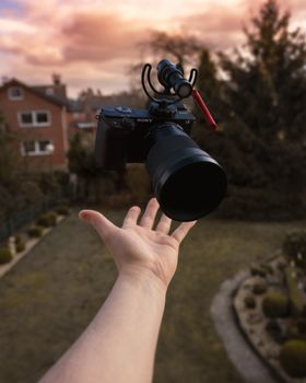 A hand appears to levitate a camera against a picturesque outdoor sunset.