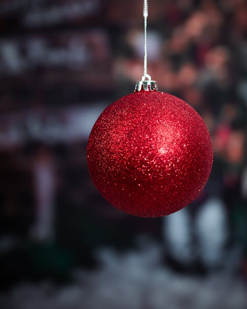 A big festive red Christmas ball, hanging by a string against a blurred, moody background, capturing the spirit of the holiday season