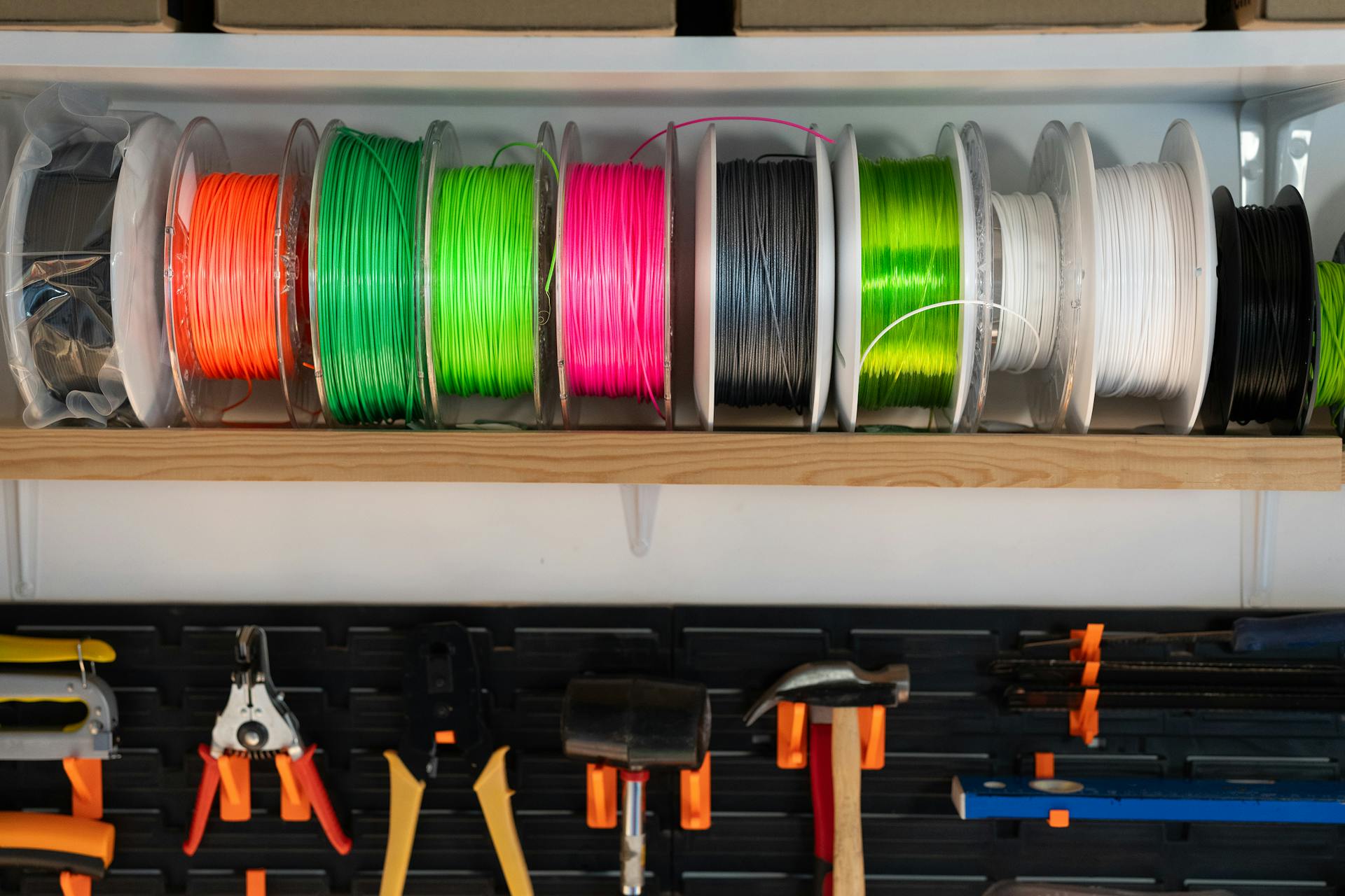 A variety of colorful filament spools and tools organized on a workshop shelf, ideal for 3D printing enthusiasts.