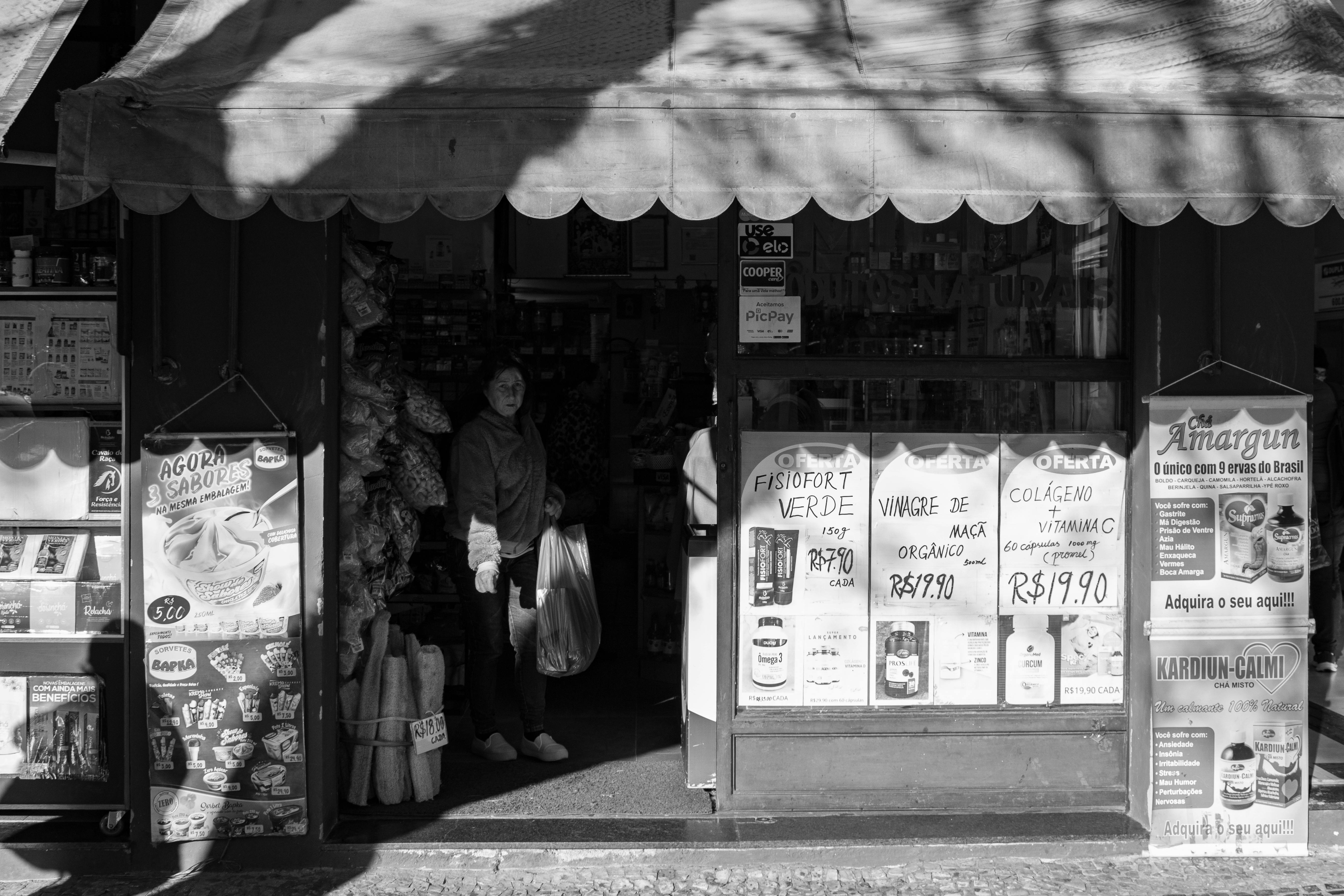 Monochrome image of a city grocery store entrance with visible signage and shadows.