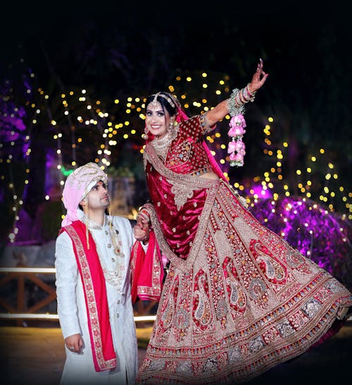 Bride and Groom in Traditional Clothing Standing on the Background of Lights and Smiling 