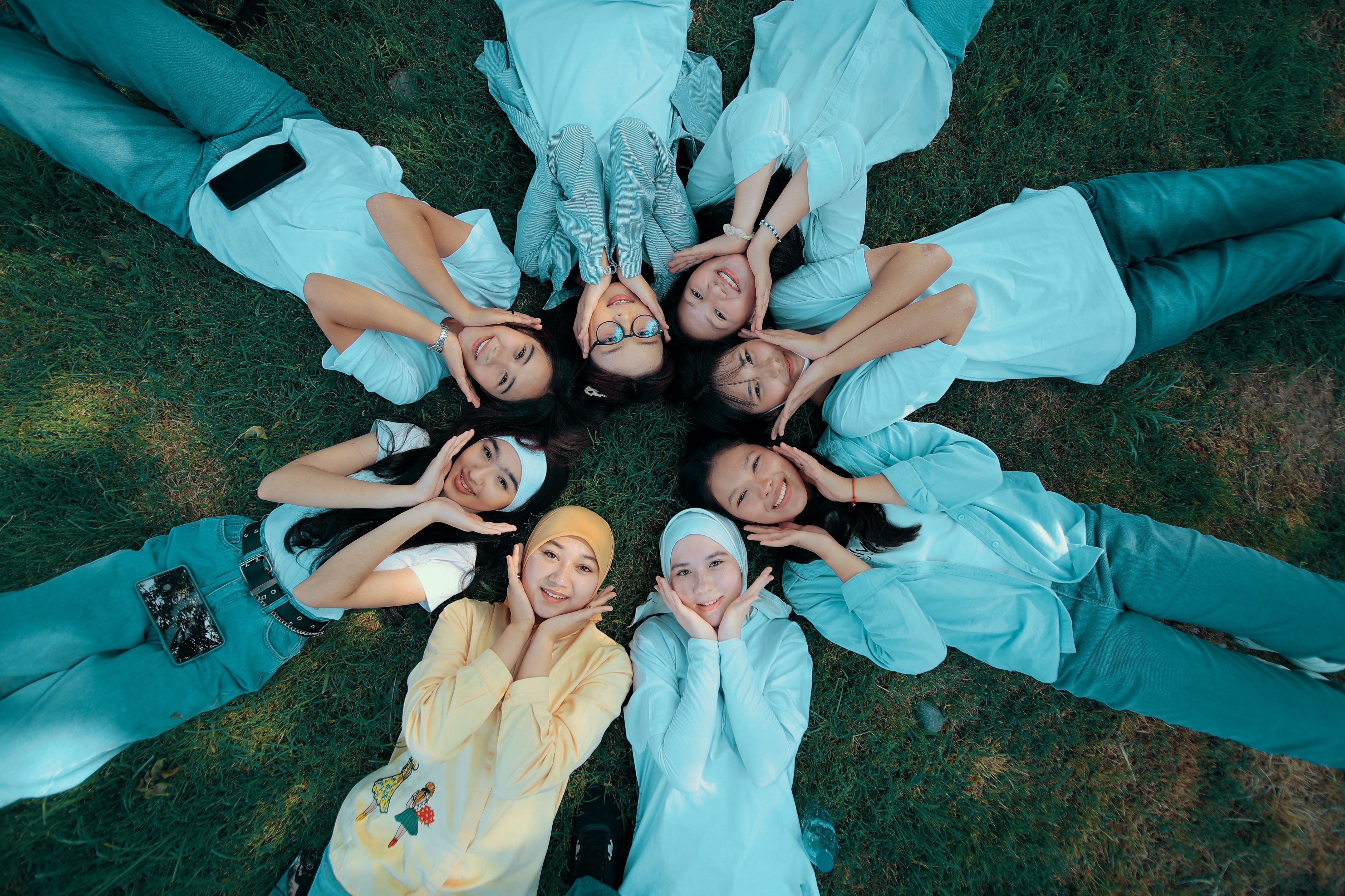 Happy group of friends lying in a circle on grass, smiling and enjoying a sunny day