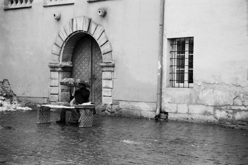A Man Sitting Outside of a Building under an Umbrella 