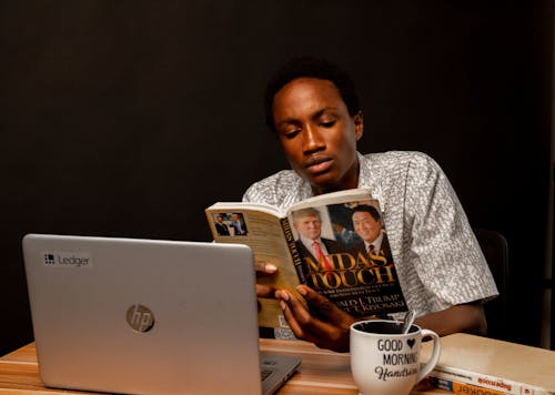 Young Man Sitting at the Desk and Reading a Book 