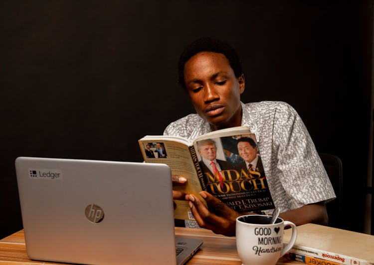 Young Man Sitting At The Desk And Reading A Book 