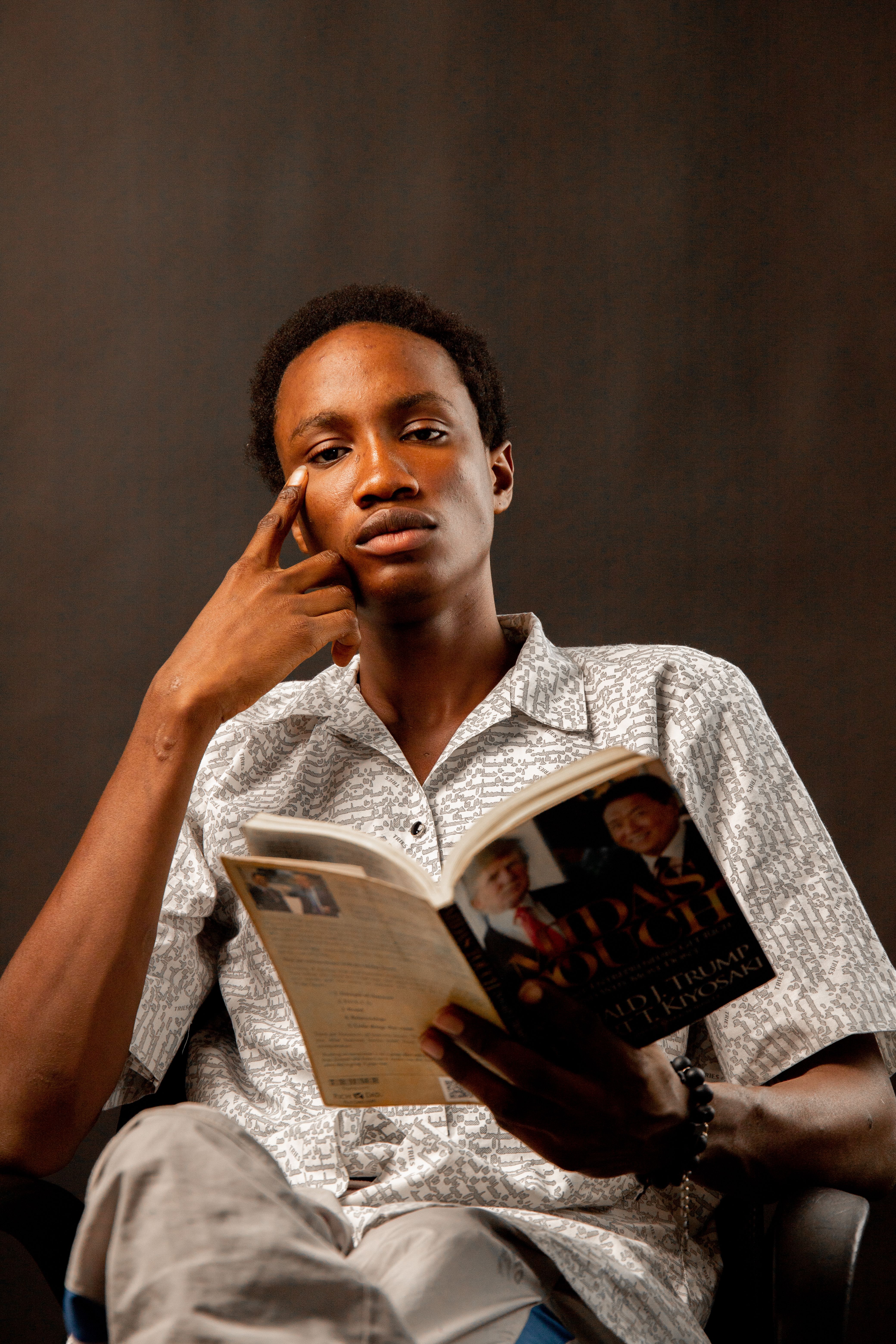 A young man deeply absorbed in reading a book while sitting indoors with a thoughtful expression.
