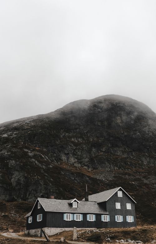 Free Scenic rural cottage beneath misty mountains in a serene landscape. Stock Photo