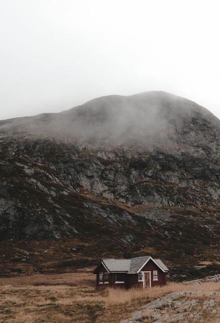 Tranquil landscape featuring a solitary cabin against a mountainous backdrop, shrouded in fog.