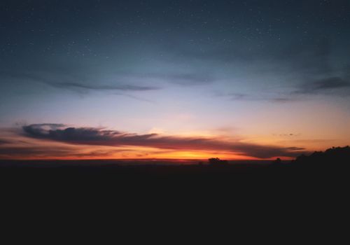 Free A tranquil landscape capturing a vibrant sunset with a starry sky during twilight. Stock Photo