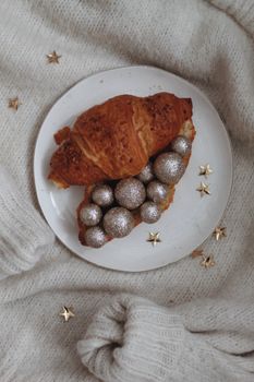 A croissant adorned with glittering spheres on a plate, perfect for a festive breakfast.
