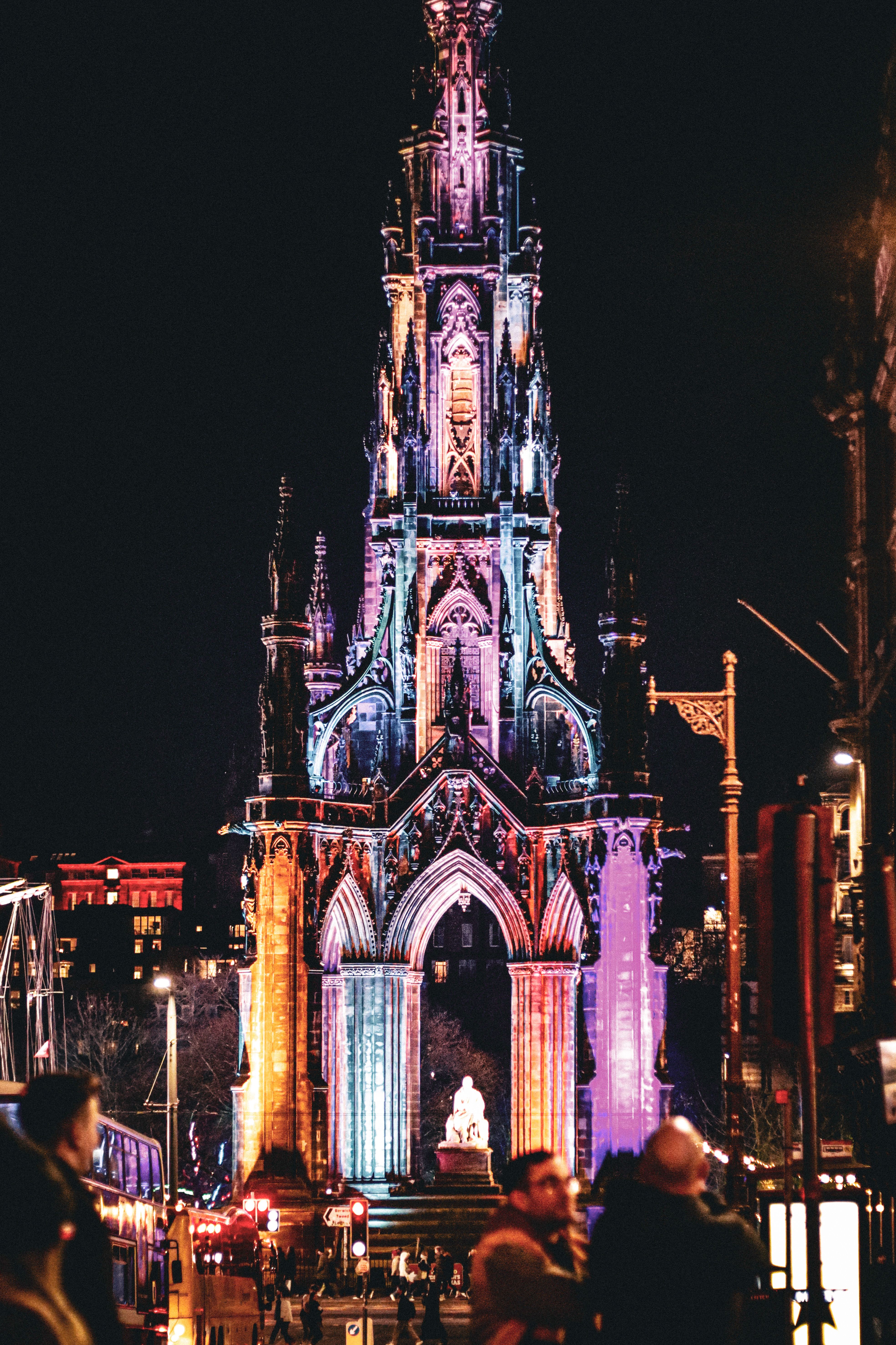 Vibrantly lit Scott Monument in Edinburgh, Scotland at night with a lively urban atmosphere.
