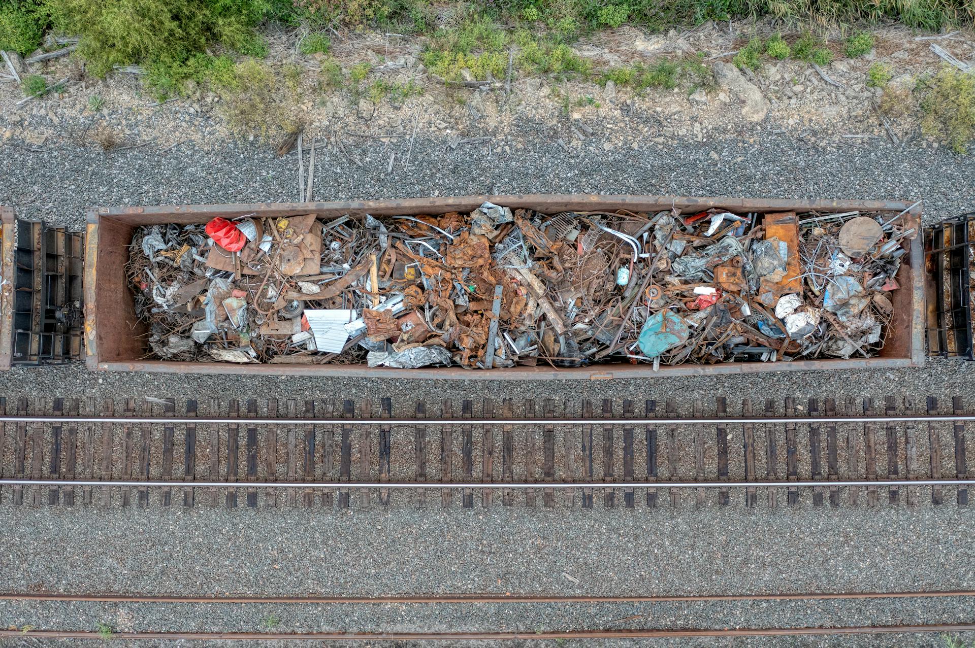 Aerial shot of an open railcar loaded with assorted scrap metal on train tracks.