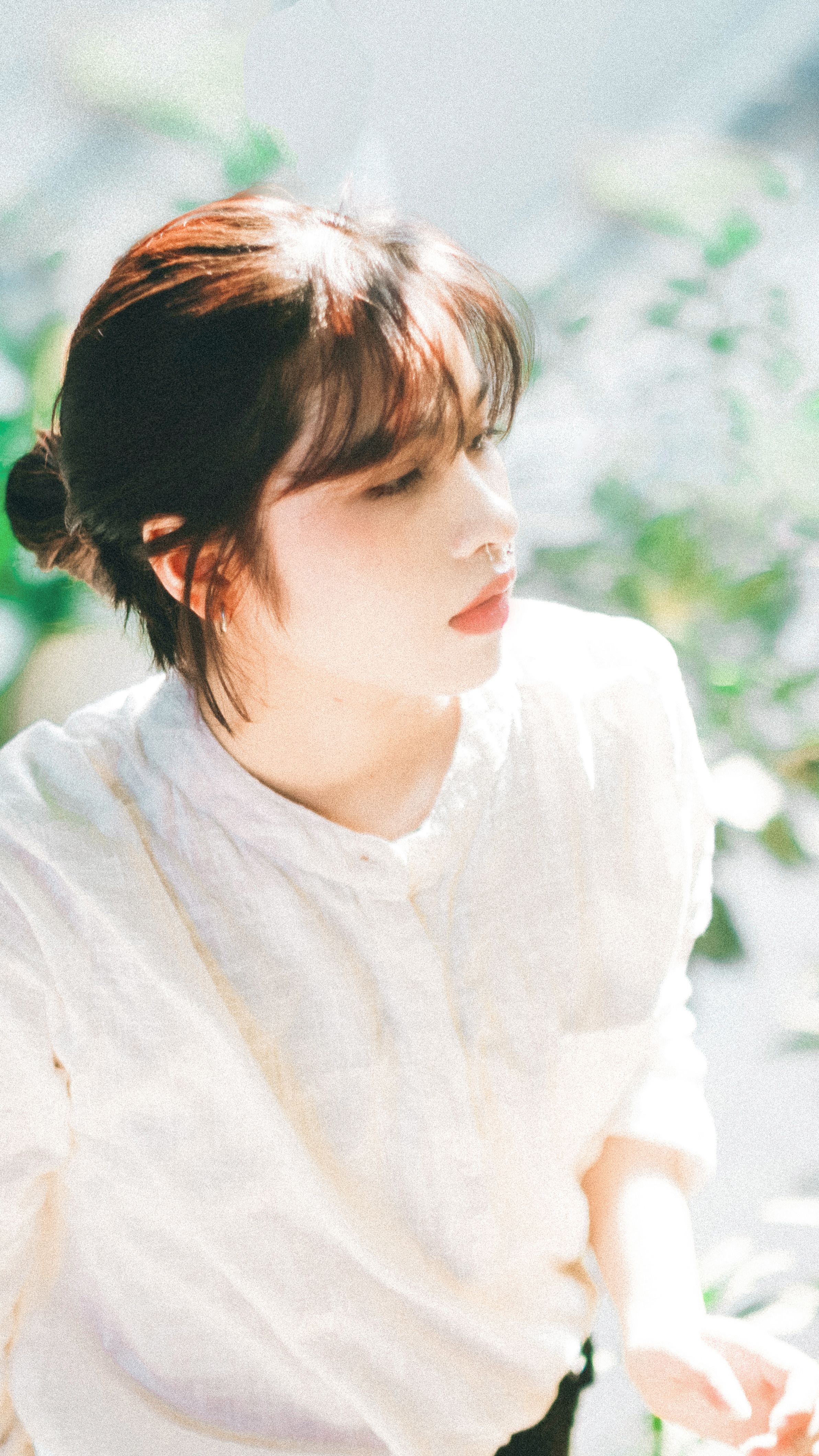 A serene portrait of a woman in soft sunlight among lush greenery.