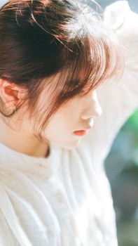 Side view of a young woman in a white blouse, bathed in gentle sunlight outdoors.