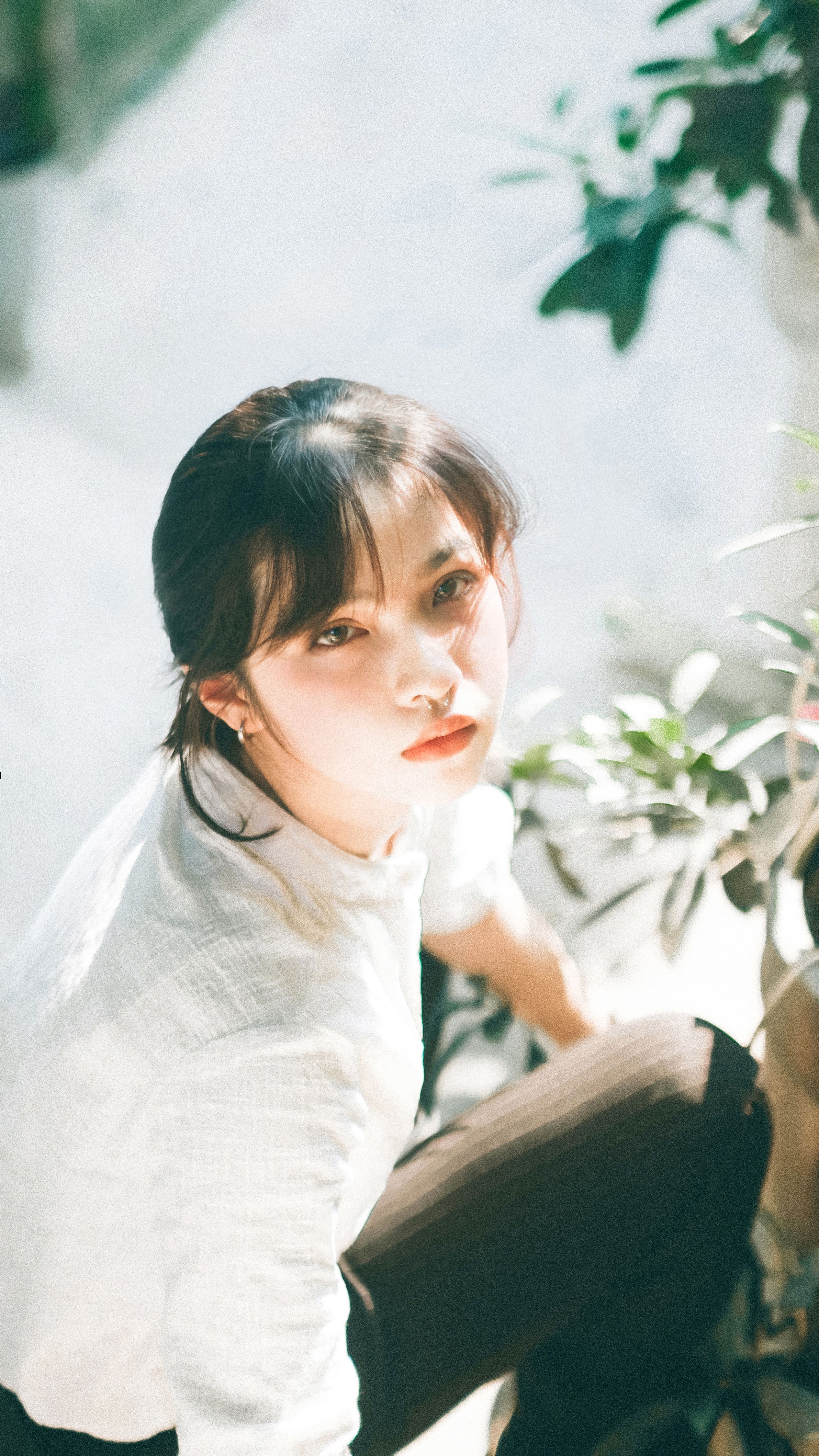 A young woman in sunlight surrounded by green foliage, looking upwards.