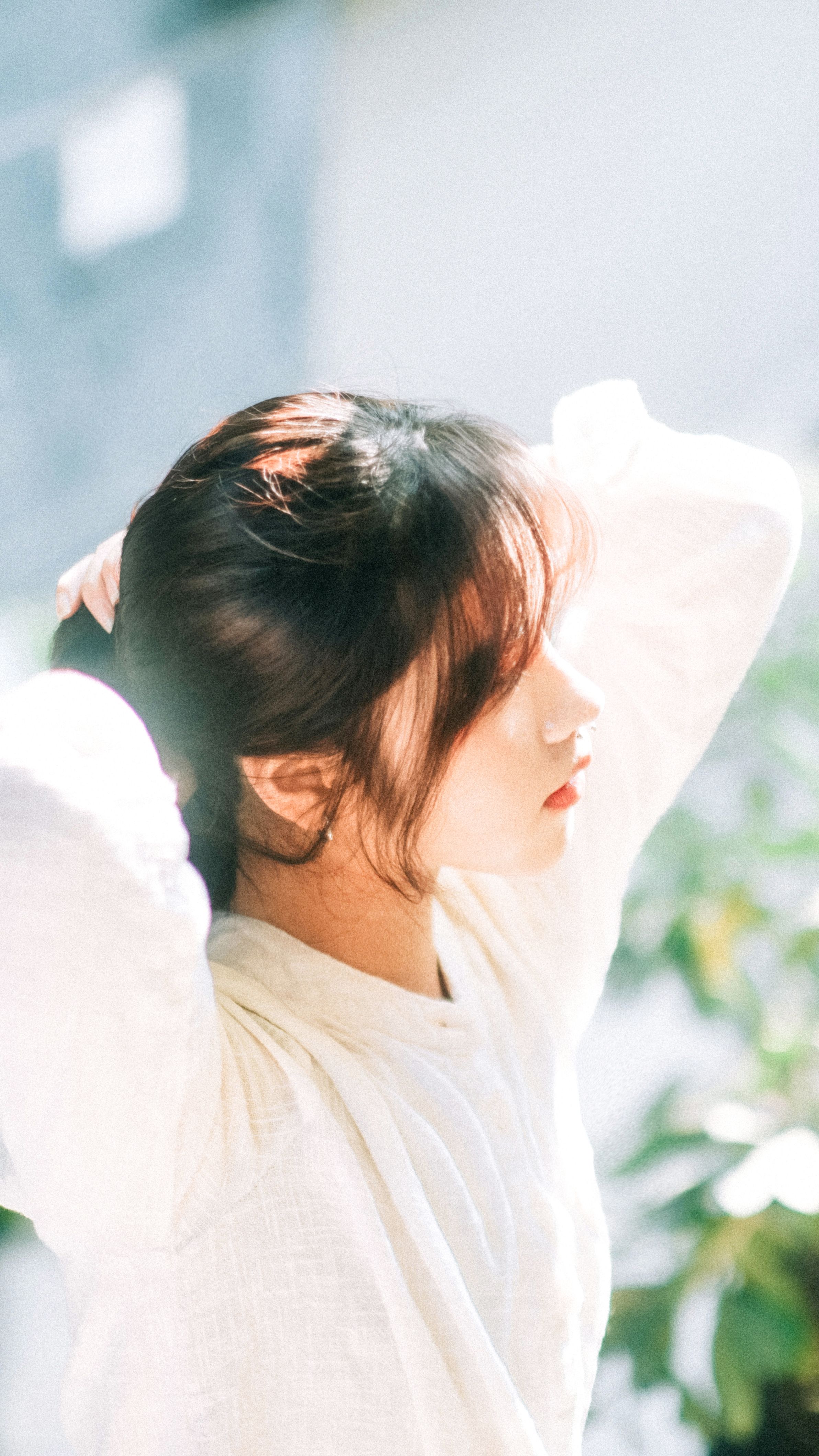 A serene portrait of a woman fixing her hair in a sunlit garden, capturing a summery vibe.