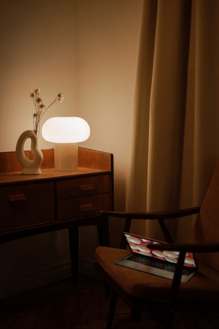 A cozy minimalist workspace with a lamp, laptop, and modern decor in a warm room.