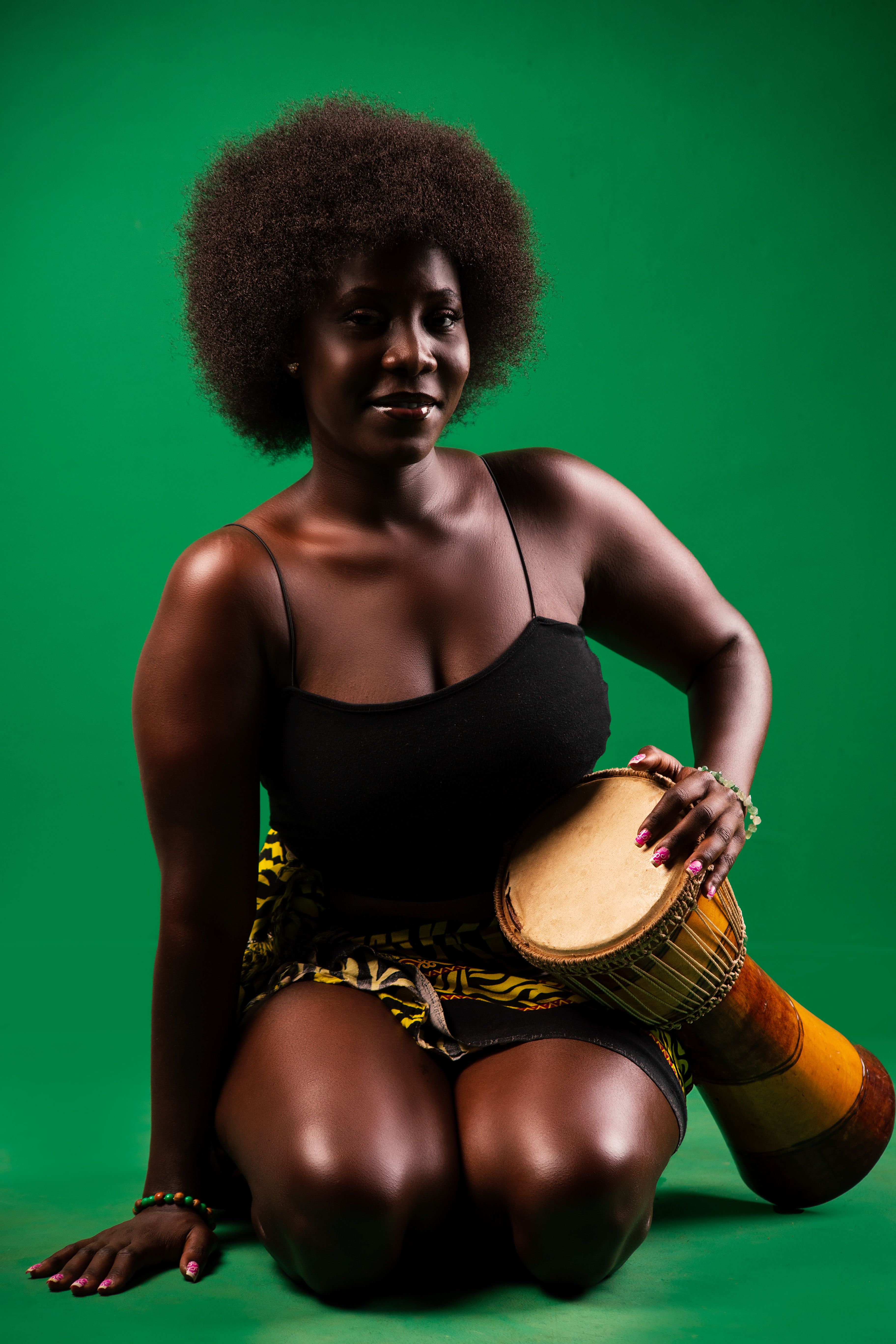 Portrait of an afro woman holding a drum against a vibrant green background in a studio.