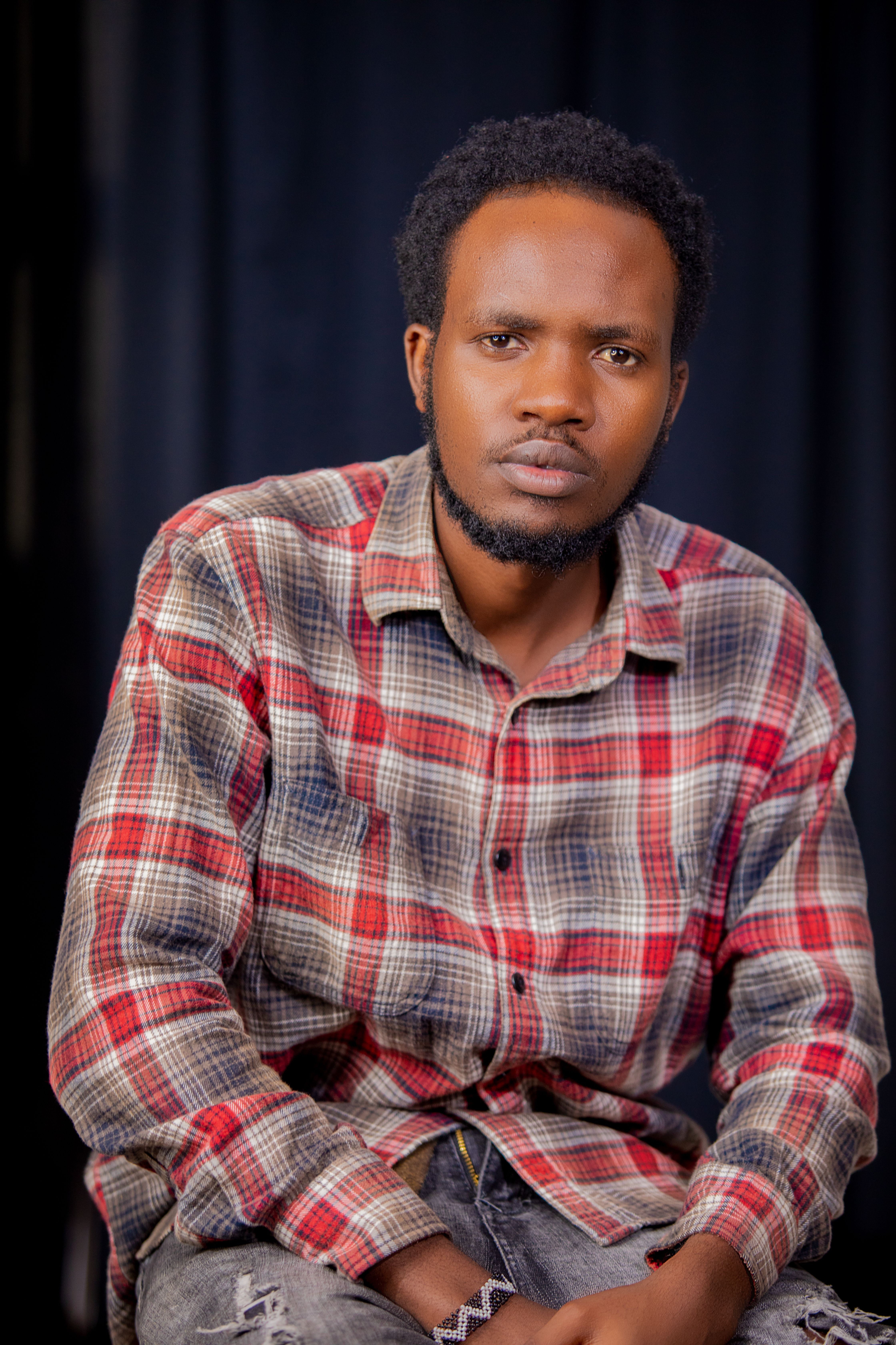 A serious man wearing a plaid shirt poses in a studio, looking directly at the camera.
