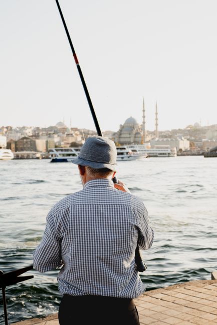 Senior man fishing with a scenic view of Istanbul's skyline and mosque in the background.