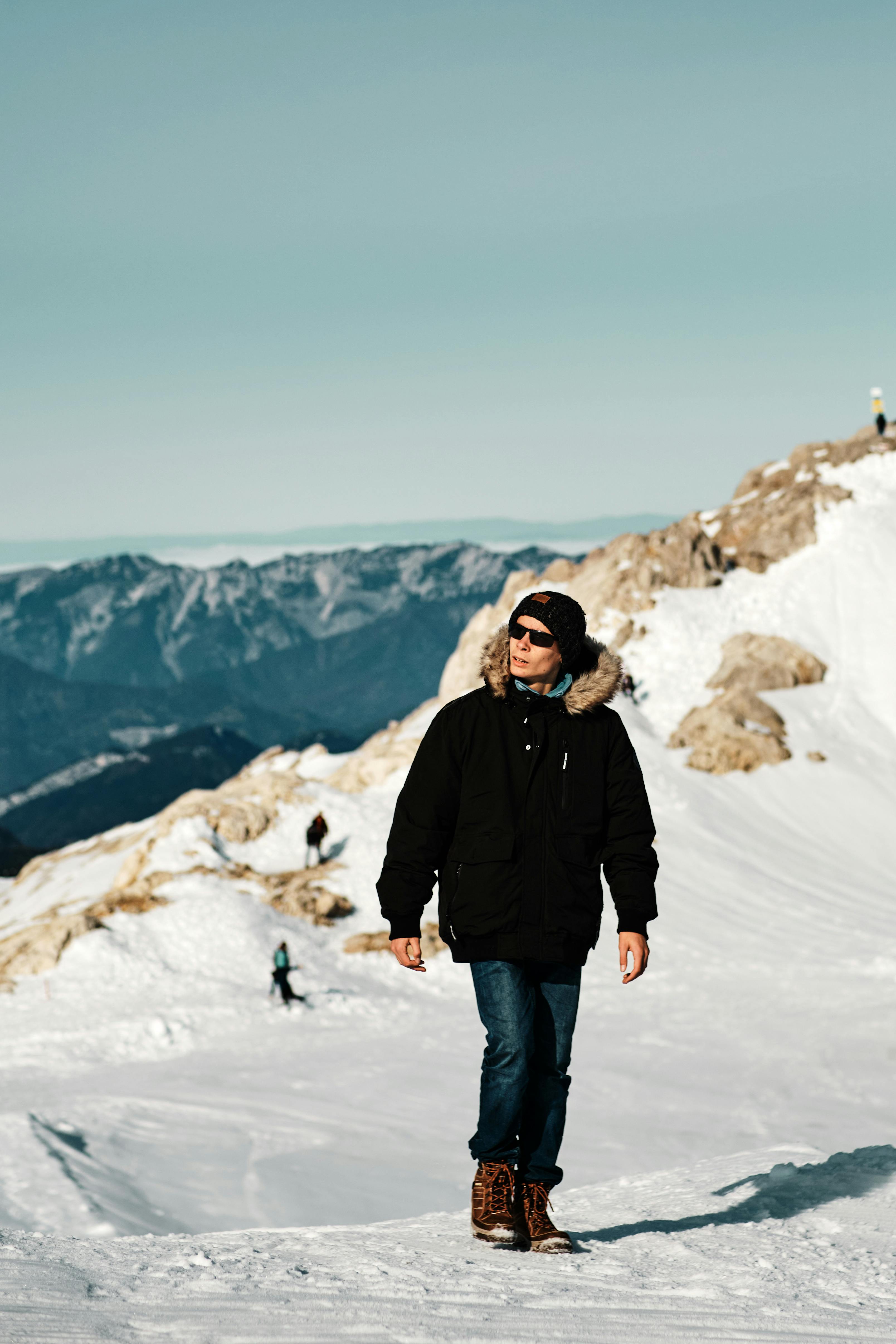 Man in winter clothing hiking on snow-covered mountains in Austria, showcasing fashion and adventure.