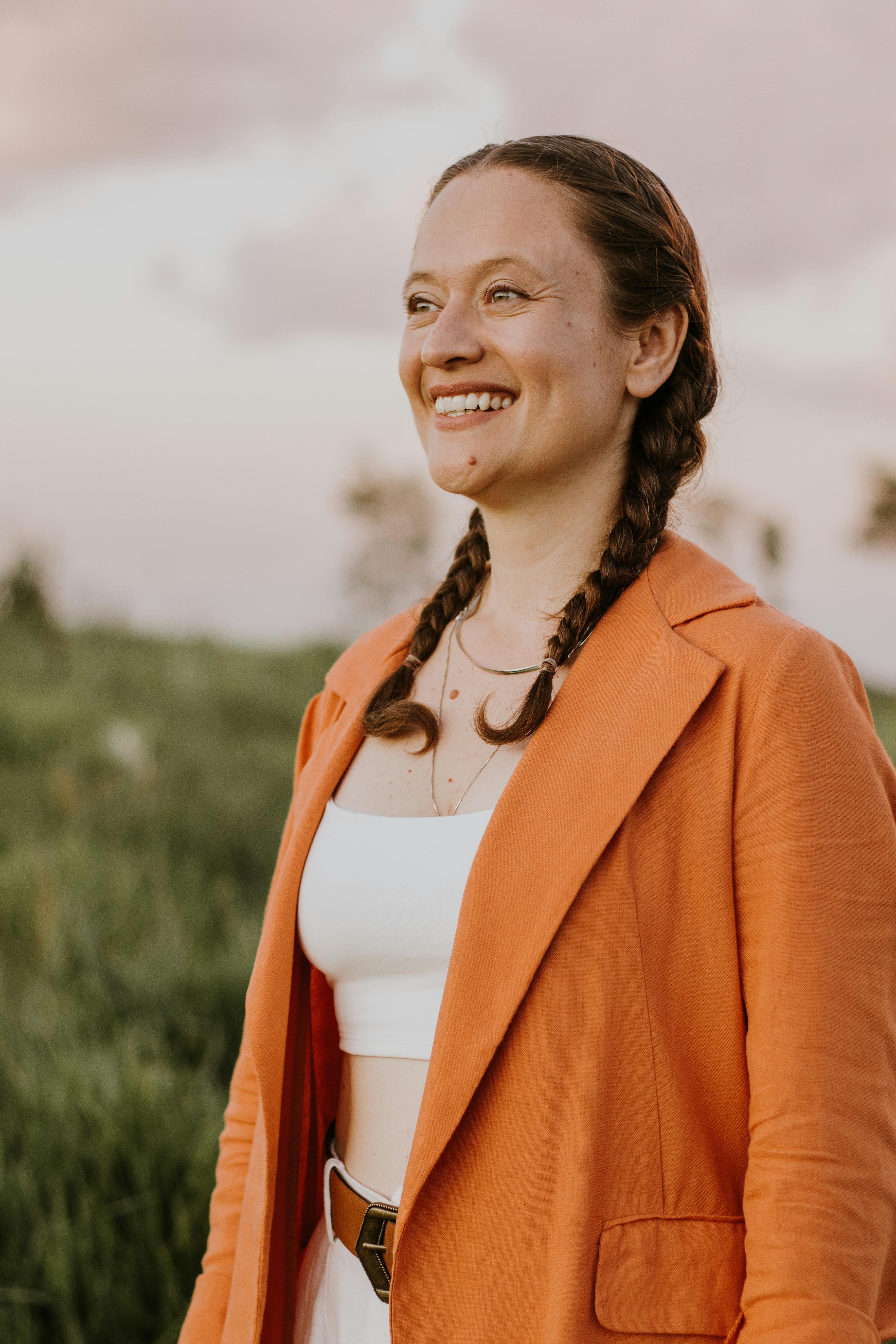 A woman in an orange jacket smiles in the middle of a field · Free ...