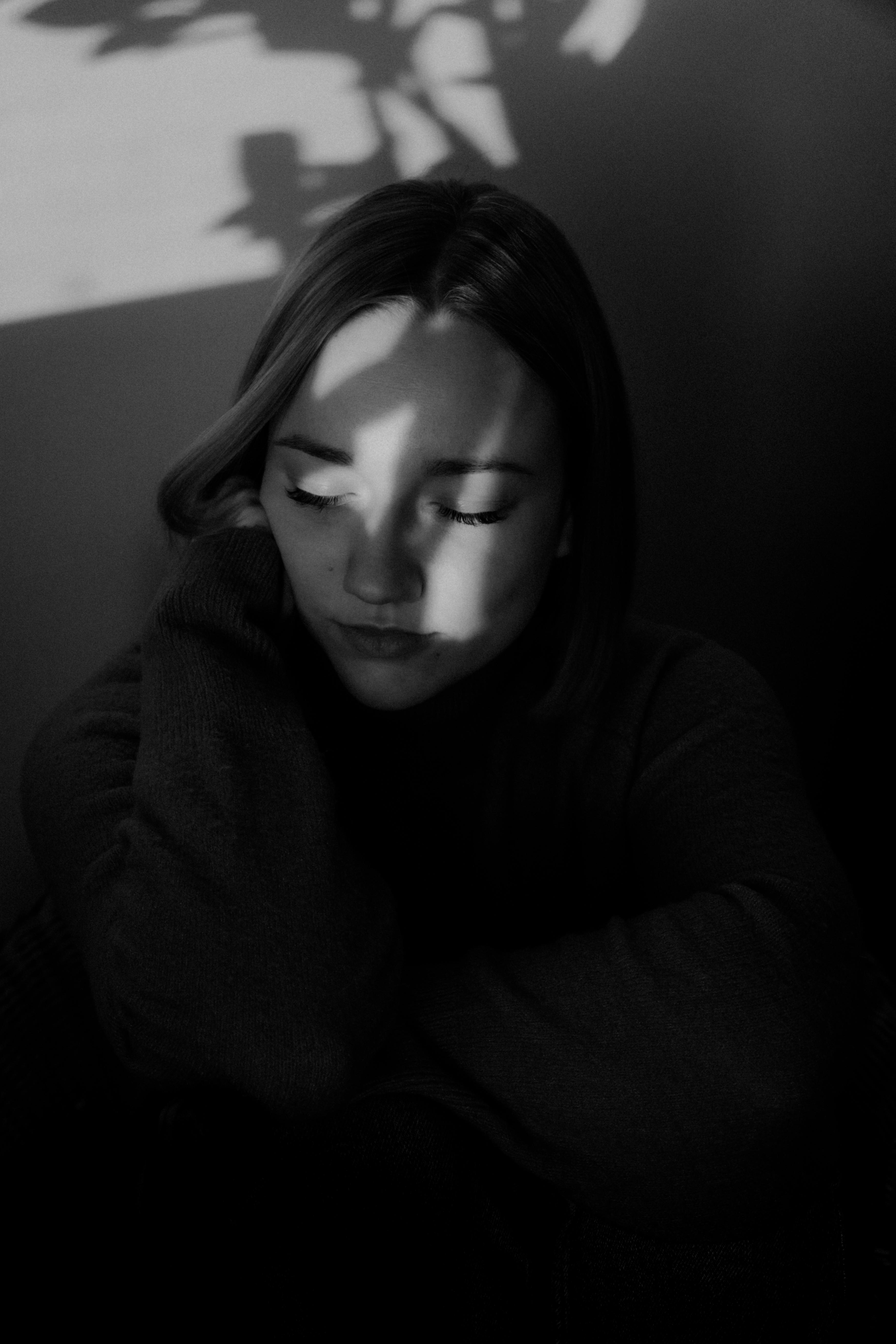 A thoughtful black and white portrait of a woman with eyes closed, enveloped in shadow.