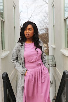 一位优雅的女人身着粉色上衣和灰色外套，在户外楼梯上摆出姿势，展现城市时尚