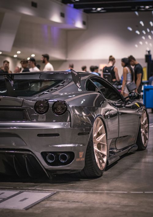 Free A stunning black Ferrari F430 displayed at an indoor motor show with people admiring the vehicle. Stock Photo