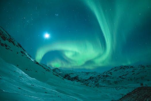 Dazzling aurora borealis illuminating the night sky above a serene snowy mountain landscape.