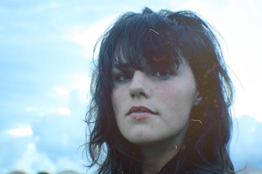 Close-up portrait of a woman with black hair against a blue sky, showcasing a serene expression.