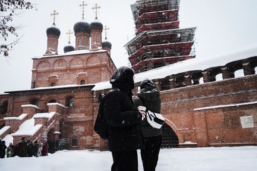 People stand outside a historic brick church in winter weather with snow falling and scaffolding visible.
