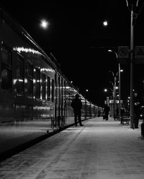 Silhouette of a man standing by a train at night, captured in black and white, exuding an urban mood.